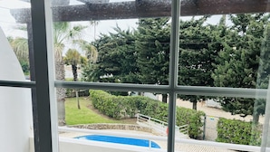 Un balcon avec des fauteuils en osier, une piscine et une vue sur la verdure et les arbres.