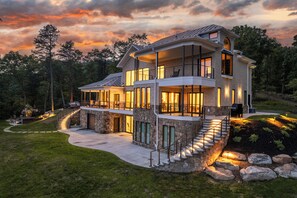 A modern two-story house with a stone foundation, large windows, and a wrap-around porch. - The Vale (Hardy County)