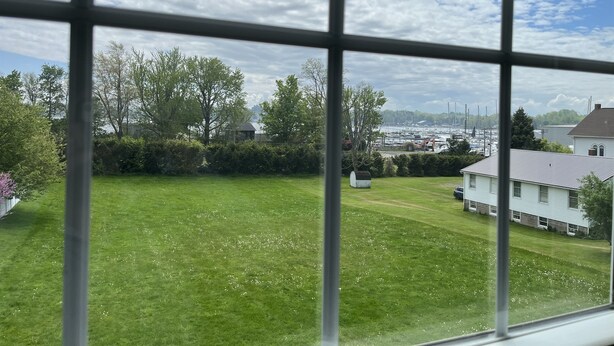 Vista a través de una ventana: un patio césped con una casa y un puerto deportivo al fondo.
