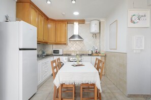 Une cuisine avec des meubles en bois, un réfrigérateur blanc, un four à micro-ondes et une cuisinière à gaz.