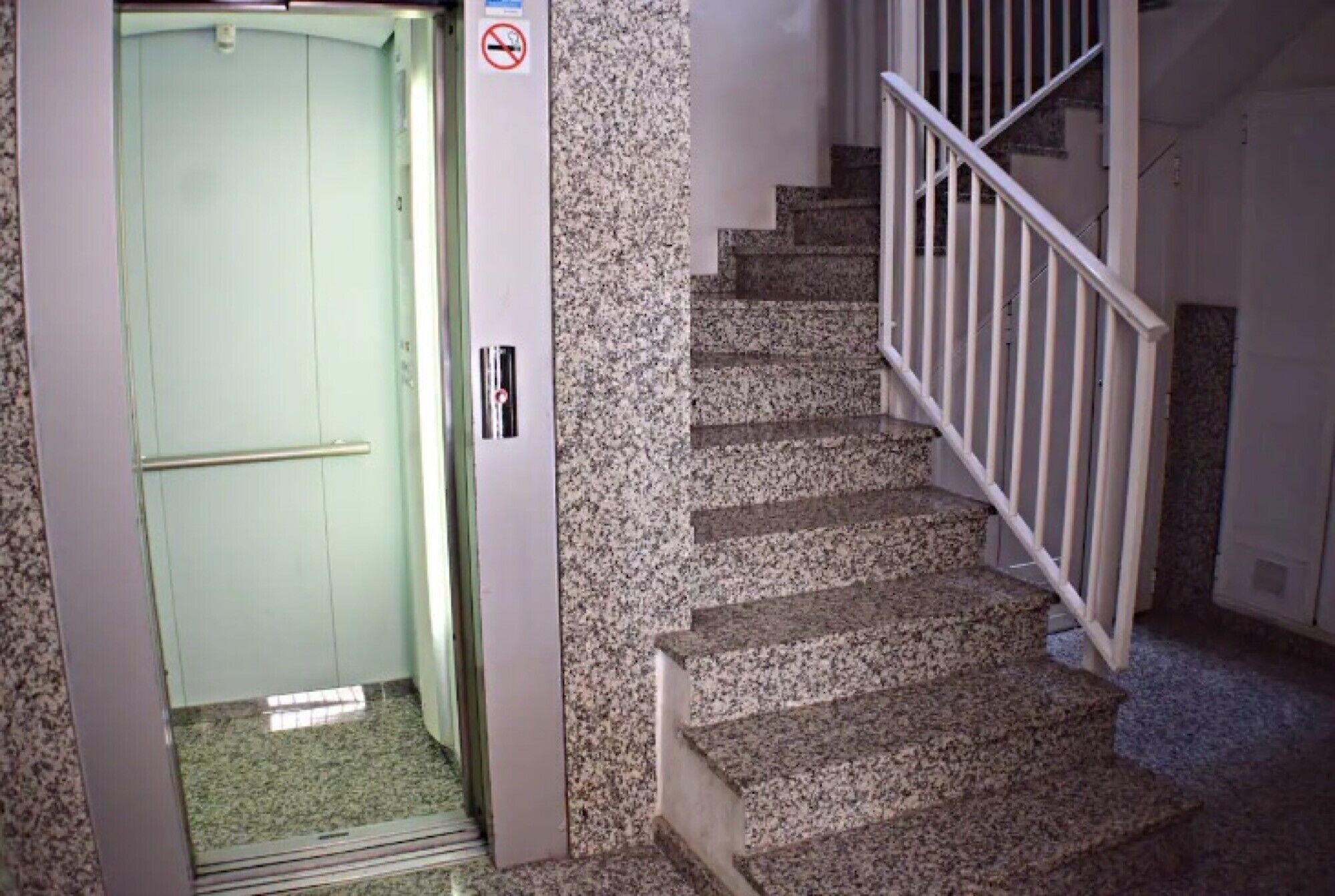 A staircase with granite steps and white railings, leading to an elevator with a green door.
