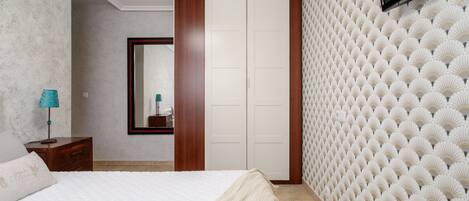 Une chambre à coucher avec un lit, une armoire, un miroir et un téléviseur.