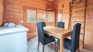 A wooden cabin interior with a dining table, four chairs, a small kitchenette, and a ladder. - Holiday Home 'Barraca Adaptado B' with Mountain View, Wi-Fi and Air Conditioning (Bárig)