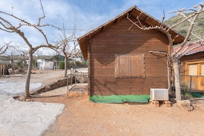 A wooden cabin with a green tarp on the ground, a small air conditioning unit, and a window with a curtain. - Holiday Home 'Barraca Adaptado B' with Mountain View, Wi-Fi and Air Conditioning (Bárig)