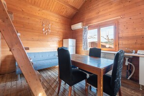 A wooden cabin interior with a dining table, chairs, a refrigerator, and a window with a view. - Holiday Home 'Barraca Adaptado B' with Mountain View, Wi-Fi and Air Conditioning (Bárig)