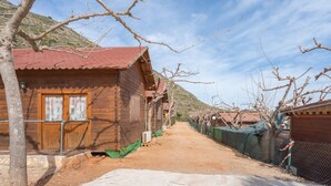 A wooden cabin with a red roof, a dirt path, and a mountainous backdrop. - Holiday Home 'Barraca Adaptado B' with Mountain View, Wi-Fi and Air Conditioning (Bárig)