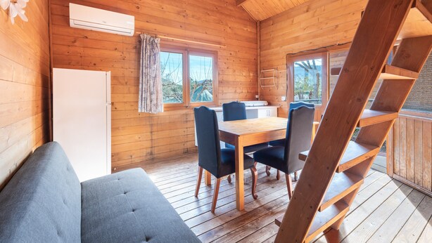 A wooden cabin interior with a dining table, chairs, a sofa, and a staircase. - Holiday Home 'Barraca' with Mountain View, Wi-Fi and Air Conditioning (Bárig)