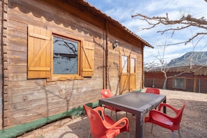 A wooden cabin with a table and chairs, a window with shutters, and a mountain in the background. - Holiday Home 'Barraca' with Mountain View, Wi-Fi and Air Conditioning (Bárig)