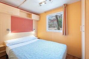 Un dormitorio con cama, ventana con cortinas, estante en la pared y lámpara de techo.