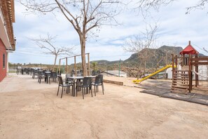 An outdoor patio with tables and chairs, a playground with a slide, and a view of hills in the background. - Holiday Home 'BW 2018 V' with Mountain View, Wi-Fi and Air Conditioning (Bárig)