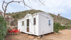 A white mobile home with a porch, a dining table with chairs, and a small garden area. - Holiday Home 'BW 2018 IV' with Mountain View, Wi-Fi and Air Conditioning (Bárig)
