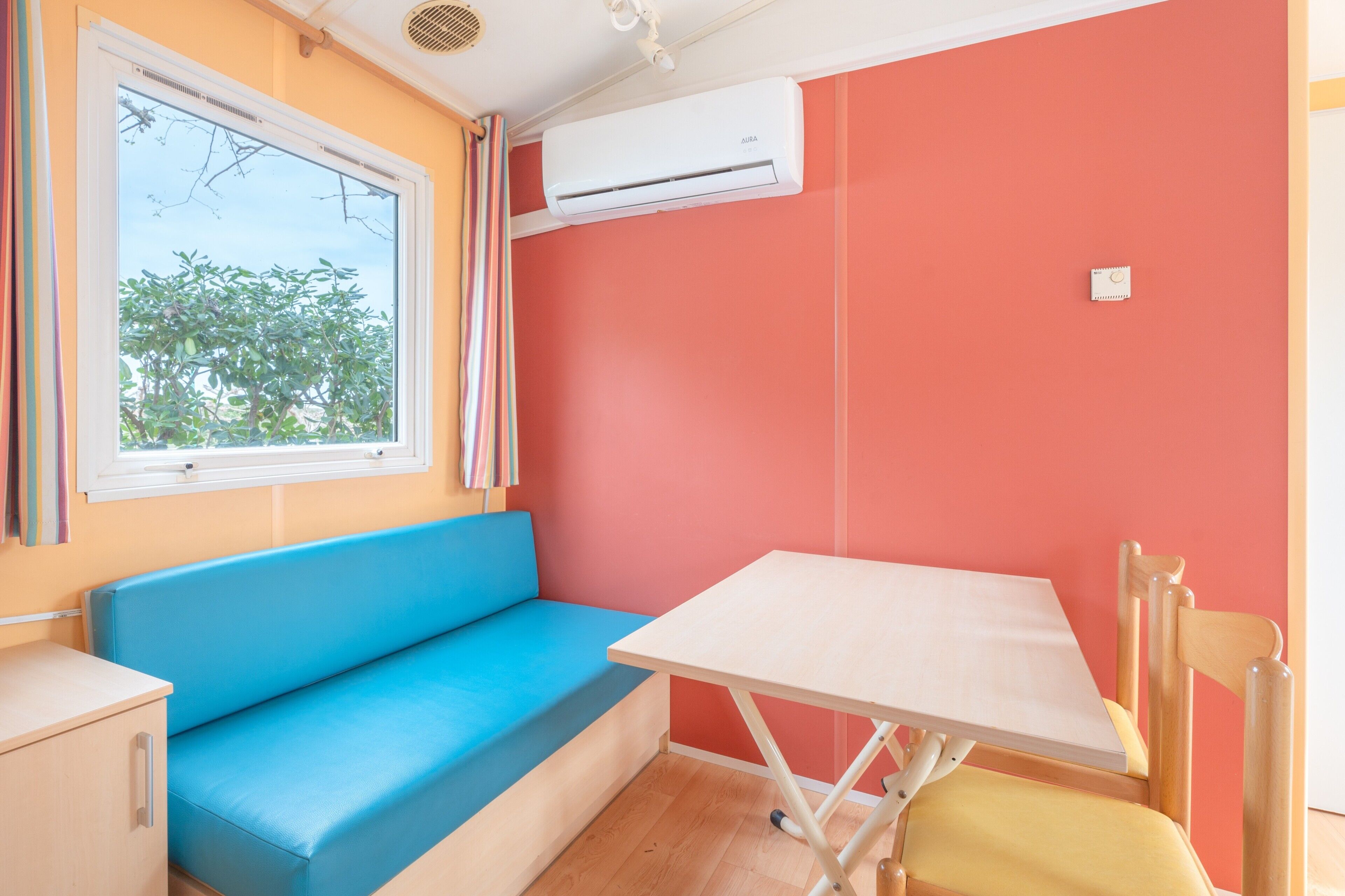 A room with a blue sofa, a small table, a wooden chair, an air conditioner, and a window with curtains.