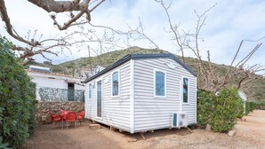 Une maison mobile avec une allée en gravier, une terrasse dotée de chaises rouges et un mur de pierres en arrière-plan.