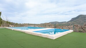 Une piscine rectangulaire entourée de gazon synthétique, avec une chaîne de montagnes en arrière-plan.