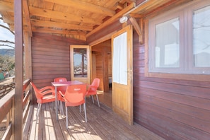 A wooden cabin with a deck, a table with chairs, and a door leading to an interior room.