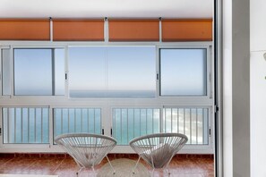 A balcony with two wicker chairs, a large window with a view of the sea, and a sliding door.
