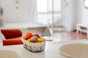 A dining table with a woven placemat, a bowl of fruit, and a red couch in the background.