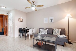 A living room with a sofa, coffee table, and a ceiling fan. There is a dining area with chairs and a table.
