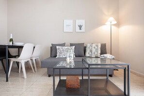 Ein modernes Wohnzimmer mit Glastisch, einer Couch mit Kissen, einem Esstisch mit Stühlen und einer Stehlampe.
