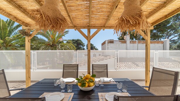 Un espace extérieur aménagé pour les repas, avec une table en bois, des chaises et un plafond en osier tressé.