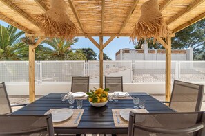 An outdoor dining area with a wooden table, chairs, and a woven ceiling.