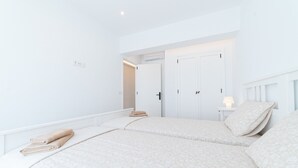 Une chambre avec deux lits, une armoire, une table de chevet avec une lampe et une porte donnant sur une autre pièce.