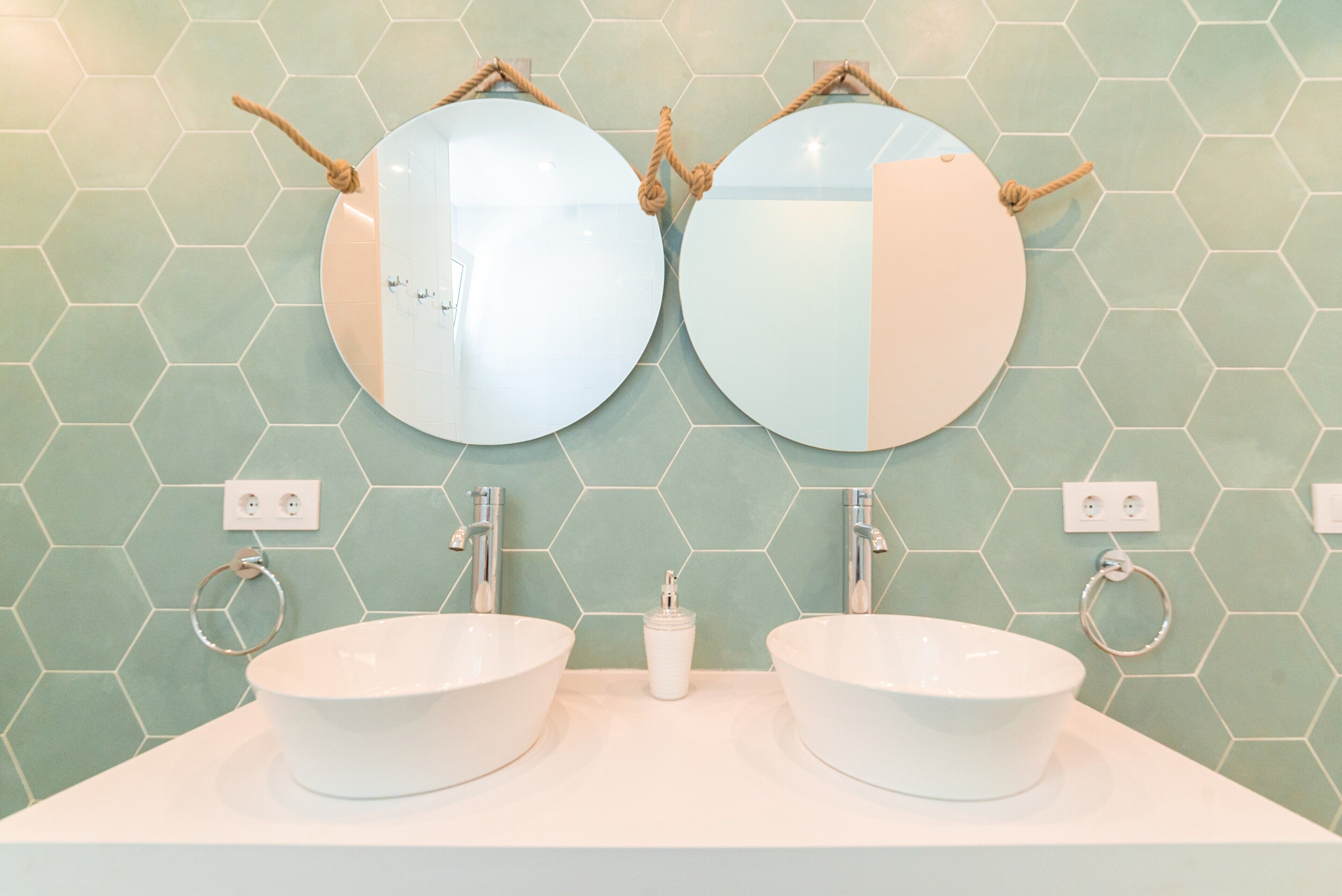 A bathroom with two round mirrors, two sinks, and a hexagonal tile backsplash.