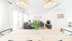 Un coin repas avec une table en bois, des chaises noires, une plante en pot, des suspensions en osier et un canapé en arrière-plan.