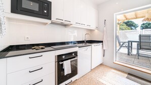 Une cuisine moderne avec des meubles blancs, un plan de travail noir, un four à micro-ondes encastré et une fenêtre donnant sur un espace patio.