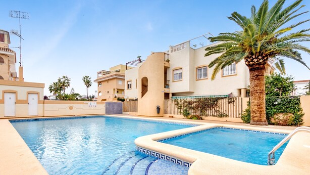 A swimming pool with a geometric tile pattern, surrounded by buildings with balconies and palm trees. - Apartment 'Casa Molins' with Shared Pool, Private Terrace and Wi-Fi (Dénia)