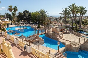 A pool area with multiple swimming pools, palm trees, and a view of the town in the background. - Holiday Home 'Roja' with Sea View, Wi-Fi and Air Conditioning (Calp)