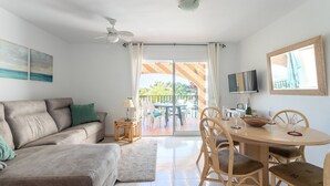 Un soggiorno con divano, tavolo da pranzo con sedie, televisione e balcone con vista.