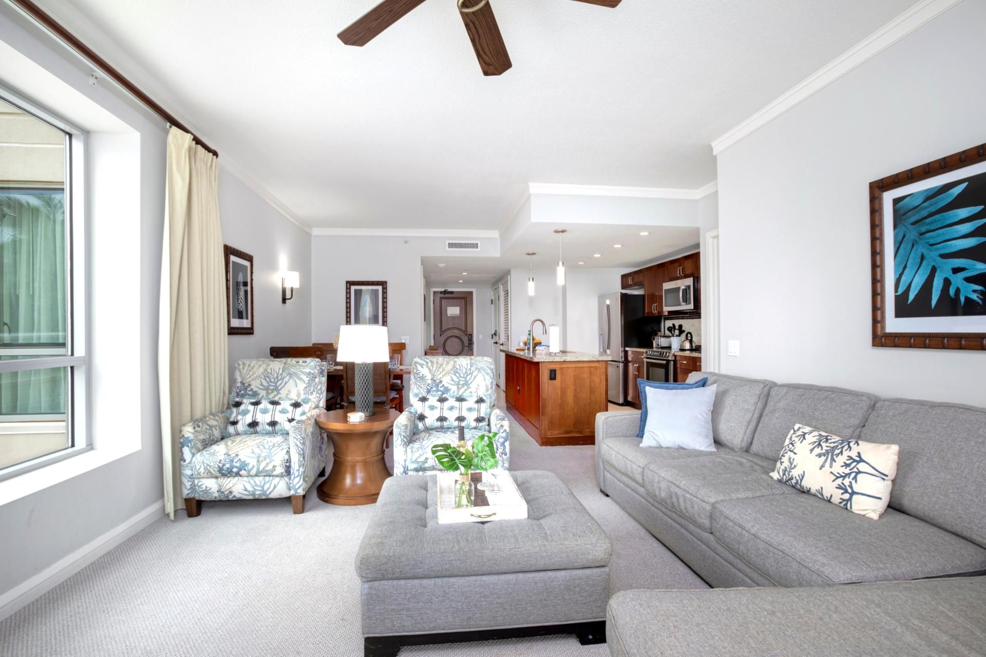 Een moderne woonkamer met een grijze bank, gestreepte fauteuils, een salontafel en een plafondventilator.
