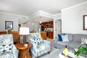 En moderne stue med en grå sofa, mønstrede lænestole, et sofabord og et spiseområde med bord og stole.