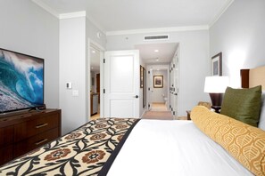 Ett hotellrum med en säng, en tv-apparat på en byrå, en hall som leder till badrummet och en dörr till köket.