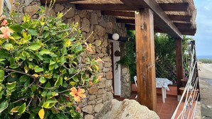 Ein Steinhaus mit einer Holzpergola, einem Tisch mit Stühlen und Blick auf das Meer.
