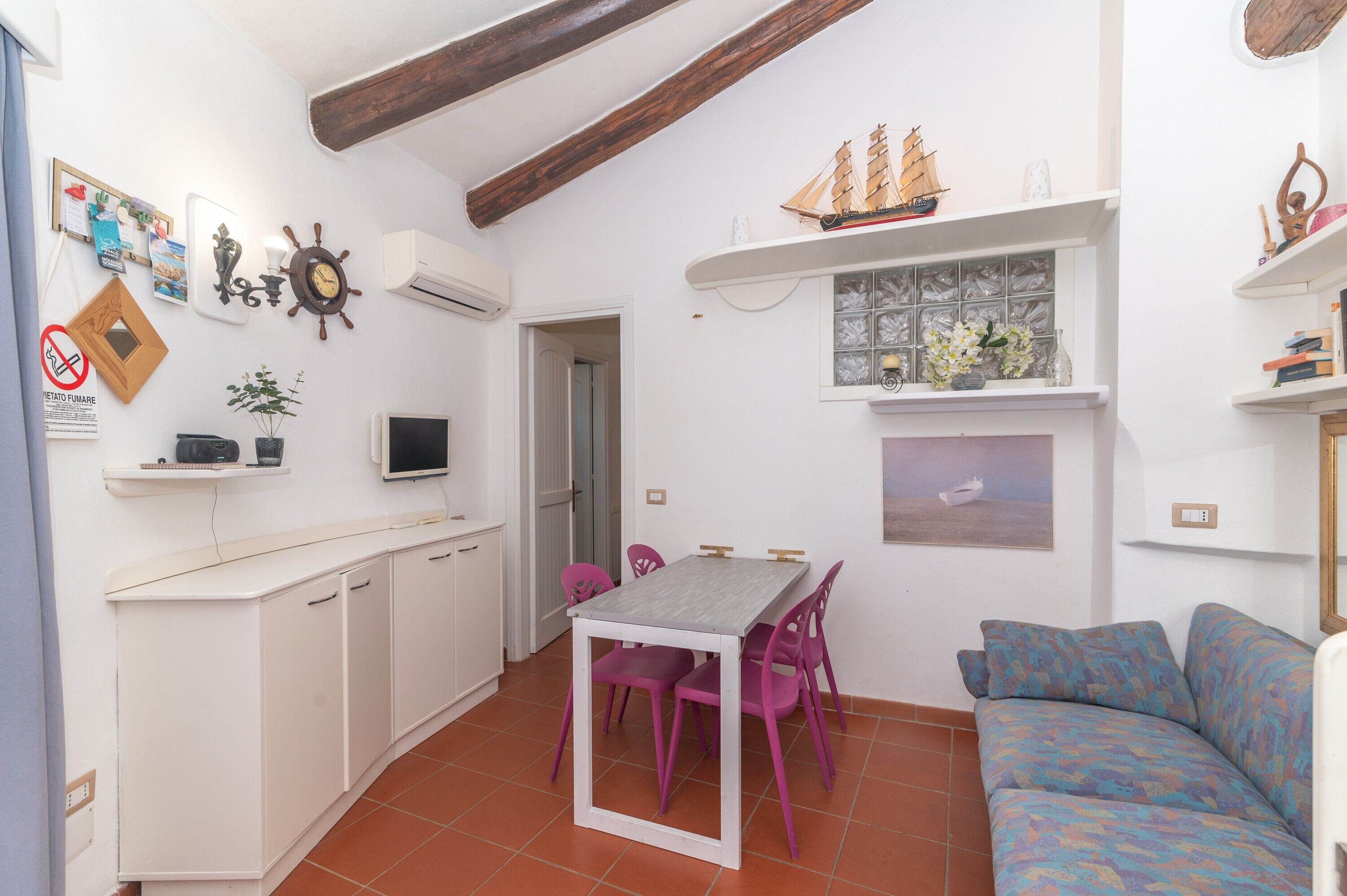A compact living space with a dining table, chairs, a sofa, a TV, and a ship model on the wall.