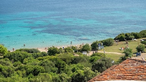 Blick auf die Küste mit klarem türkisblauem Wasser, einem Strand und üppiger Vegetation.