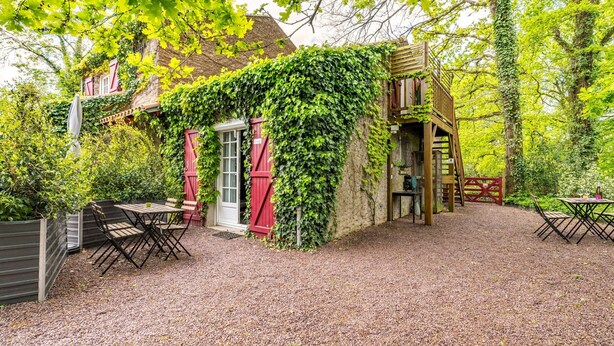 A rustic outdoor seating area with a gravel ground, a wooden table, and a red door. - Cottage 'Les Gîtes Du Robelier - L'étang' with Private Terrace, Shared Garden and Wi-Fi (Bouaye)