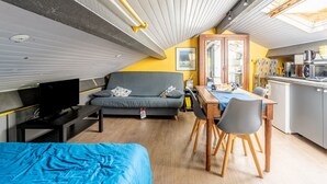 Un espai habitable compacte amb un sofà, una taula de dinar, una televisió i una cuineta.