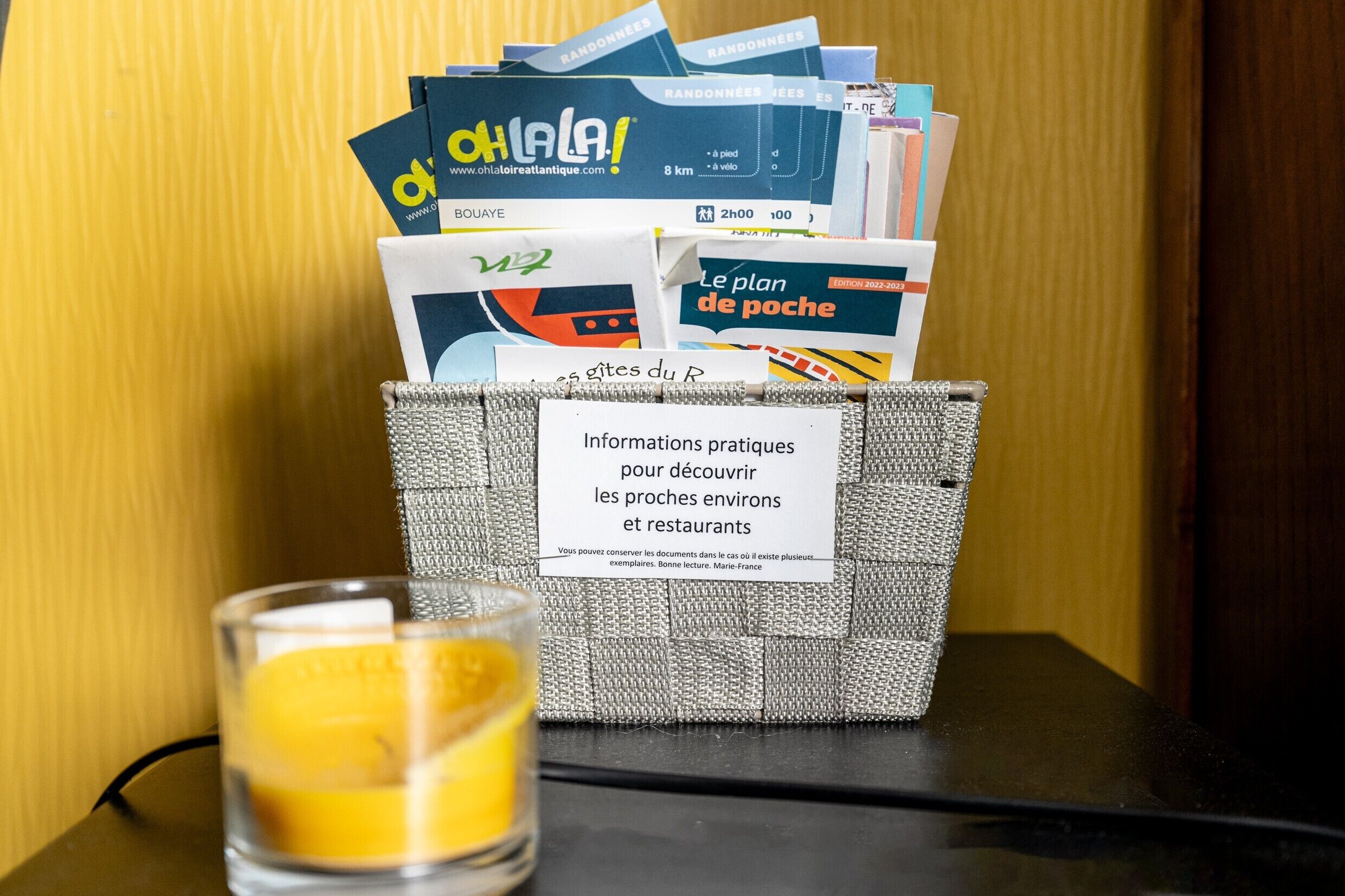 Una cesta con folletos turísticos y un vaso de jugo de naranja sobre una mesa.