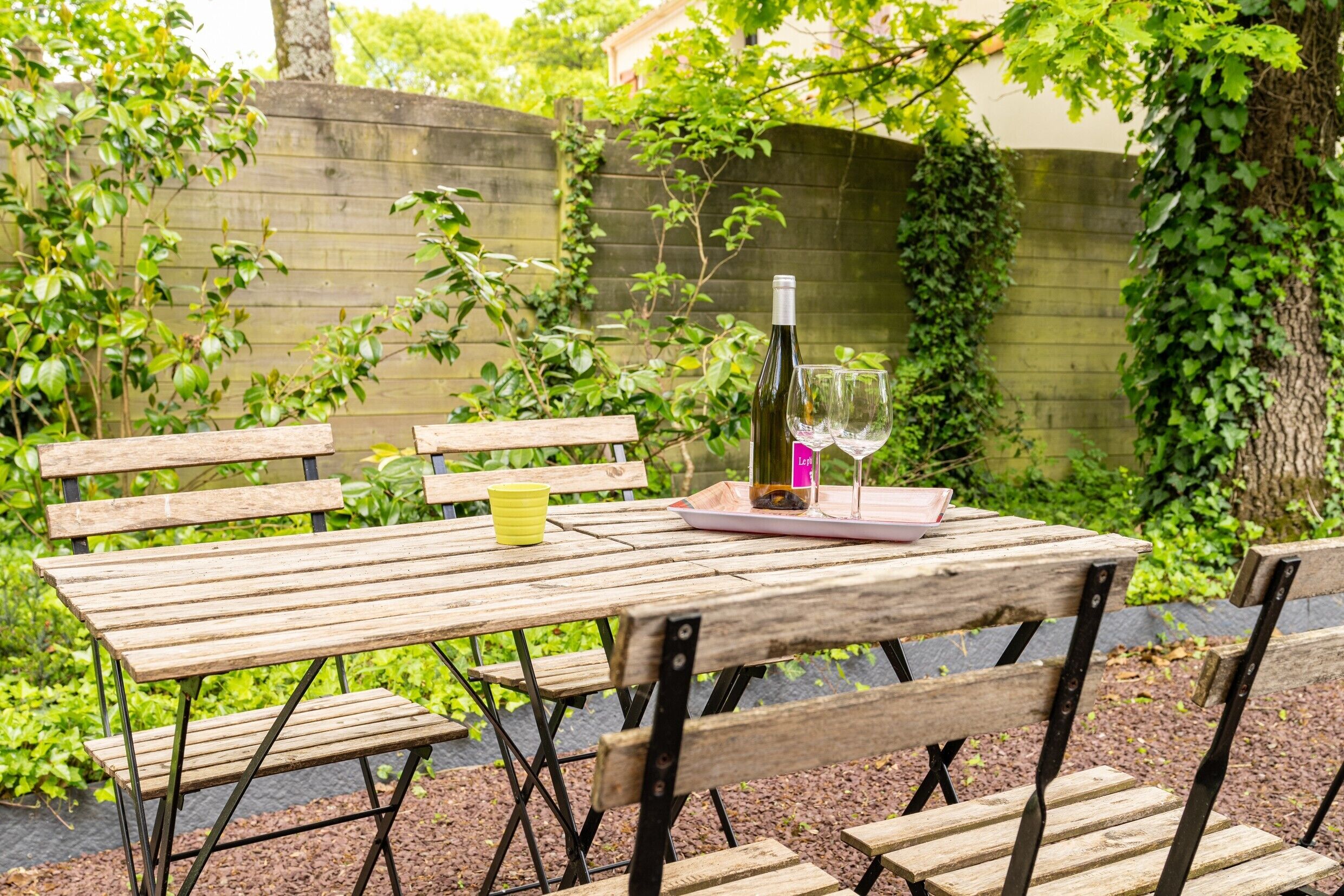 Una mesa de madera con bancos, una botella y un vaso en un jardín.