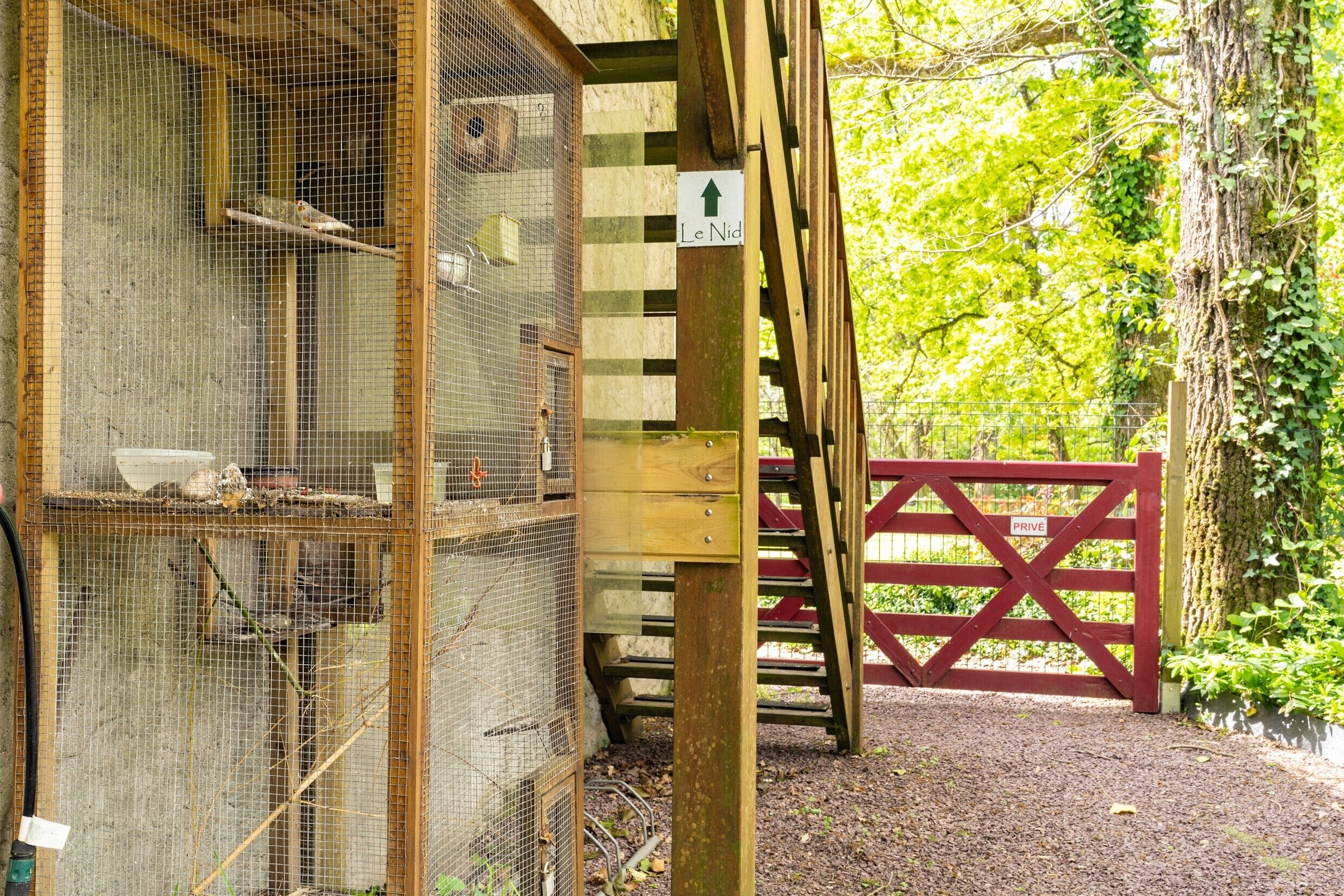 Une structure en bois agrémentée d’une volière métallique, d’une porte rouge et d’une enseigne indiquant « Le Nid ».