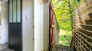 Una terrassa de fusta amb vistes a un jardí, una porta vermella i una porta corredissa de vidre.
