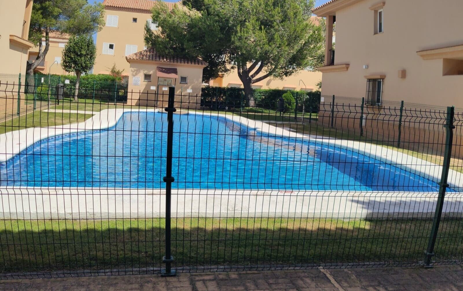 Ein Schwimmbecken, umgeben von einem Zaun, mit Gebäuden im Hintergrund.