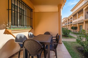 A balcony with a table and chairs, a window with bars, and a building with balconies in the background. - Apartment 'Altamar' with Shared Pool, Wi-Fi and Air Conditioning (Urbanización Novo Santi Petri)