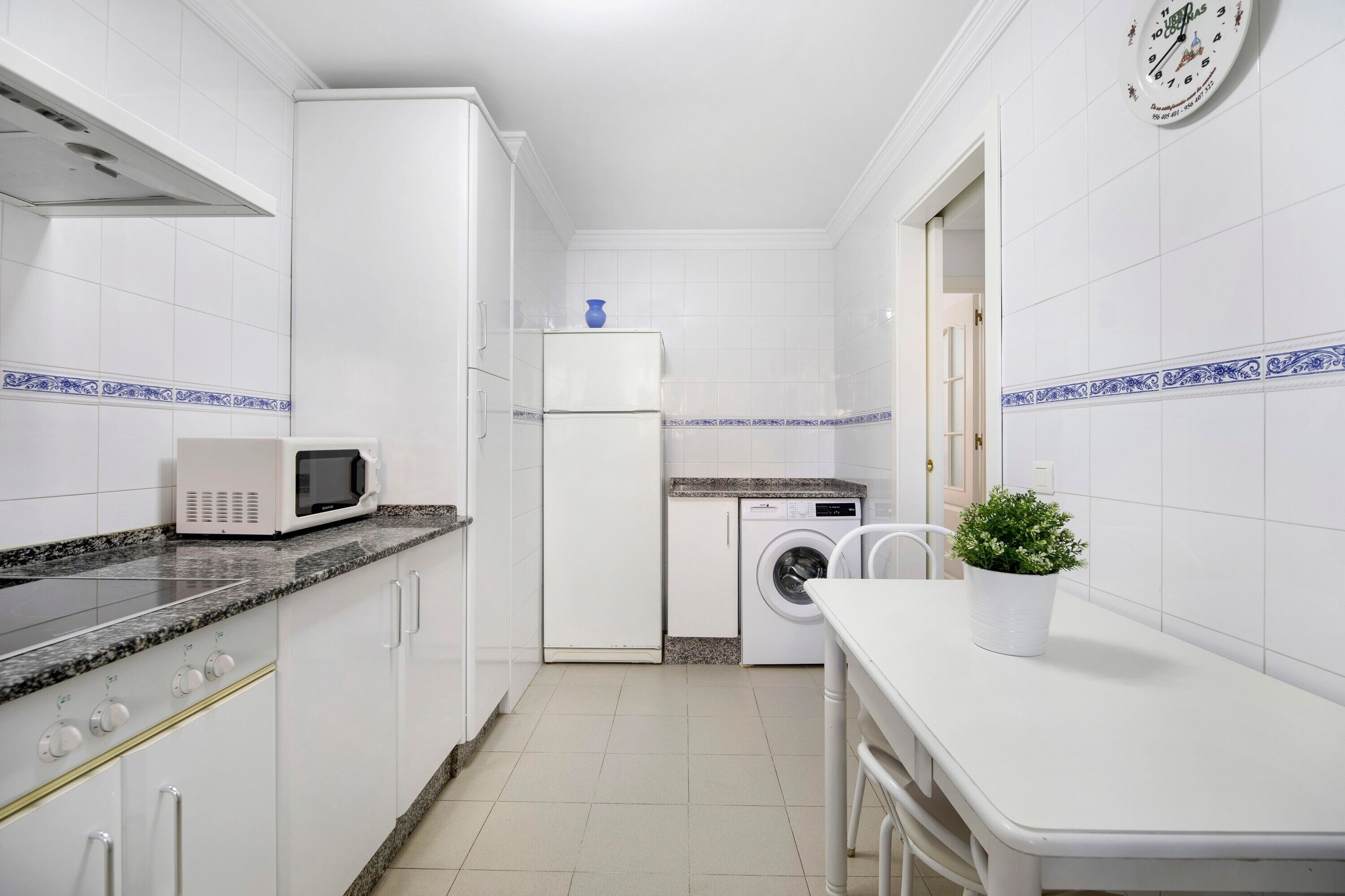 A compact kitchen with white cabinets, a microwave, a refrigerator, a washing machine, and a sink.