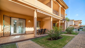 Un edificio residencial con un porche cubierto, mobiliario exterior y un pequeño jardín.