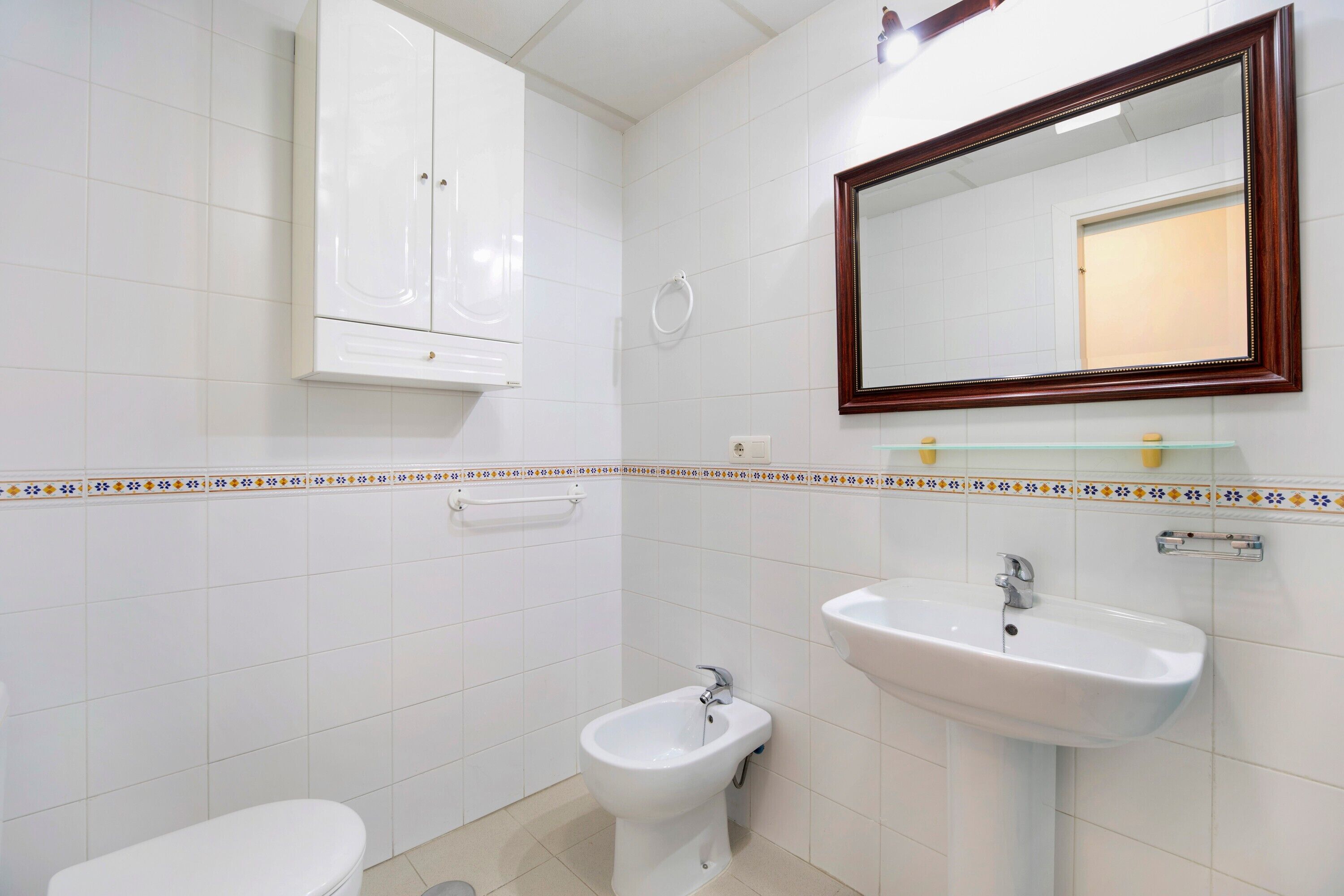 A bathroom with a toilet, bidet, sink, mirror, and cabinet.