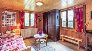 Une pièce de cabane en bois comprenant un lit, une table avec un vase, un banc et une grande porte en bois.